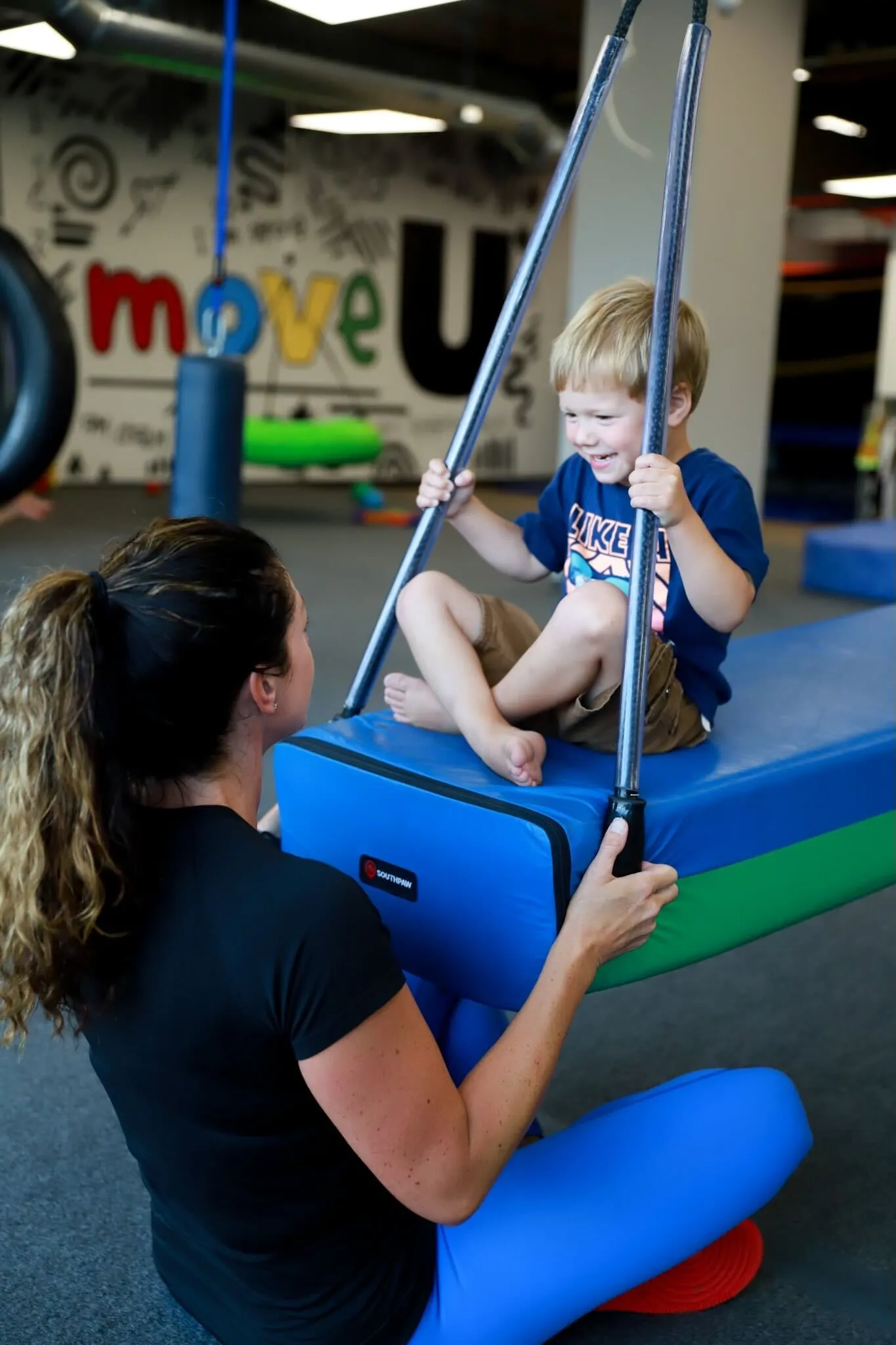 Child enjoying a swinging activity with a therapist in a pediatric therapy setting, emphasizing sensory engagement and play-based learning for school readiness.