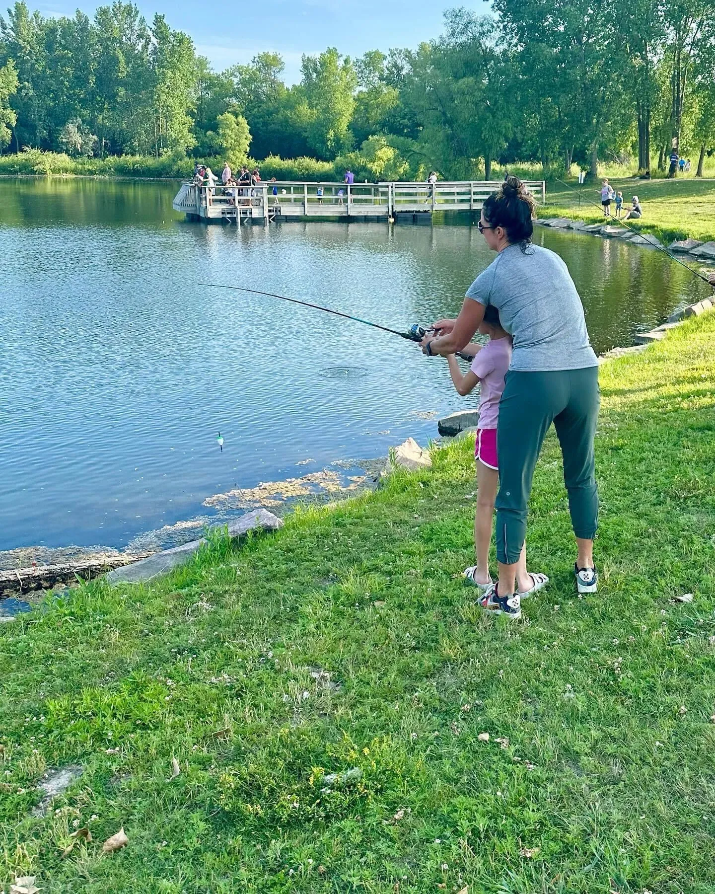 Woman and child fishing by a pond, enjoying outdoor spring activities, surrounded by nature and greenery, illustrating family bonding and sensory experiences.
