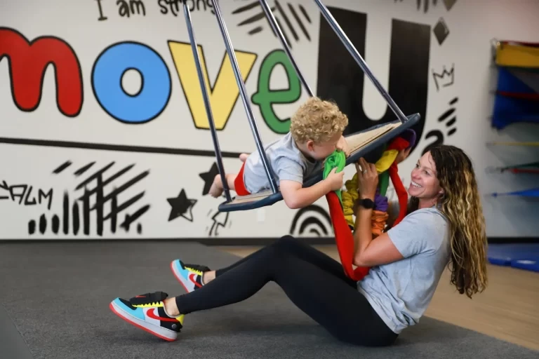 Child swinging with therapist in colorful therapy environment, promoting pediatric development at The Move U.